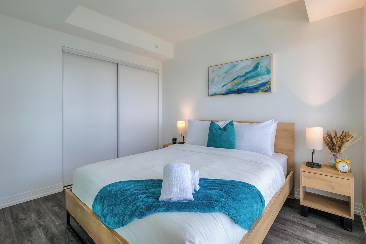 Een hotelkamer met een bed, nachtkastje, lamp, schilderij en een deur.