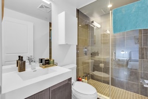 Une salle de bain moderne avec une douche à parois de verre, un lavabo blanc agrémenté d'une touche dorée et un grand miroir.