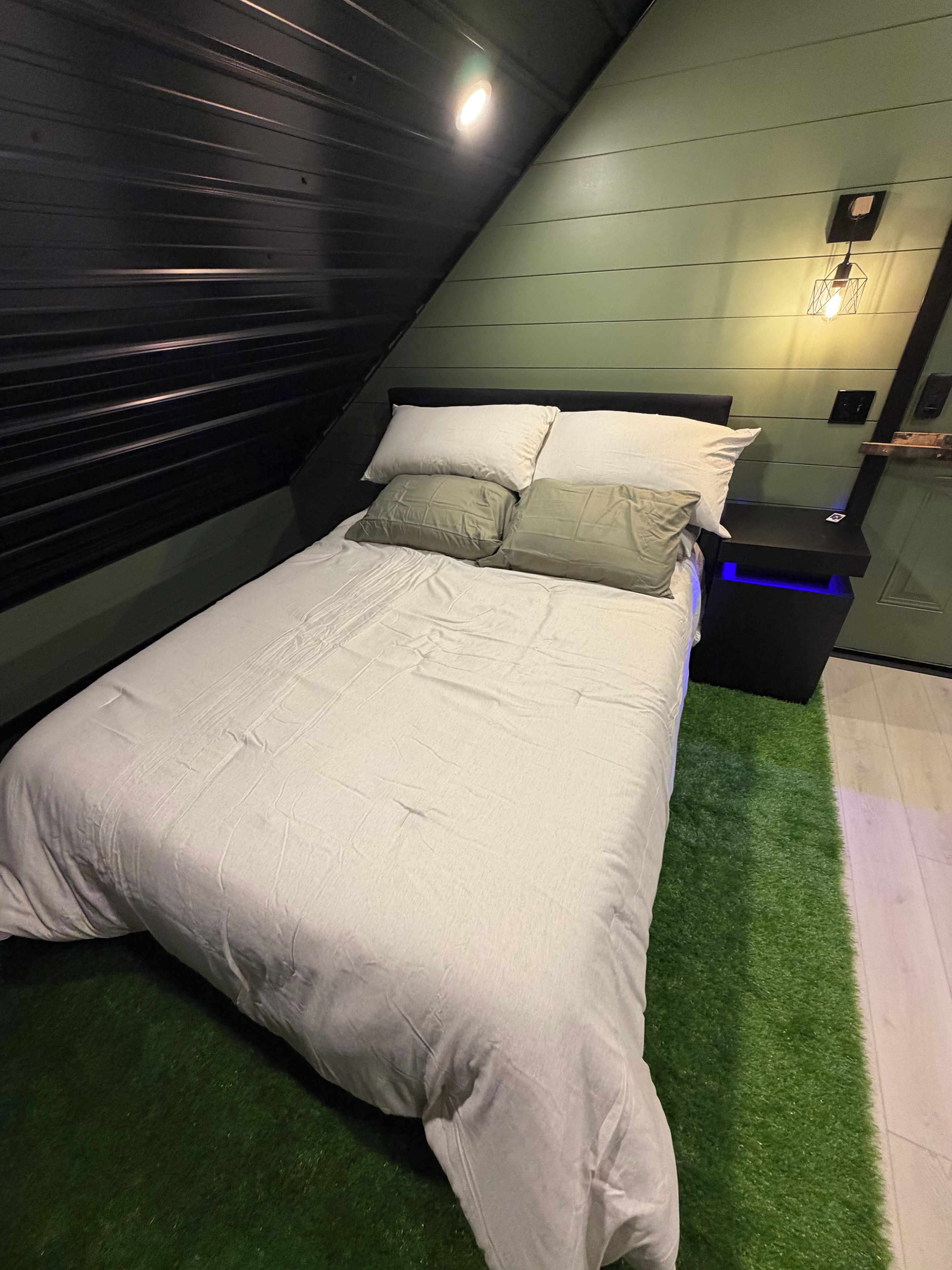 A modern bedroom with a bed, pillows, a bedside table, and a wall-mounted light fixture.