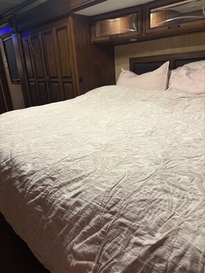 Cama com cobertura branca texturizada, cabeceira de madeira e luminária fixada na parede acima.