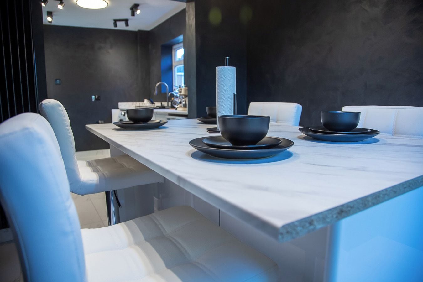 A modern dining area with a long table, white chairs, and black bowls on plates.