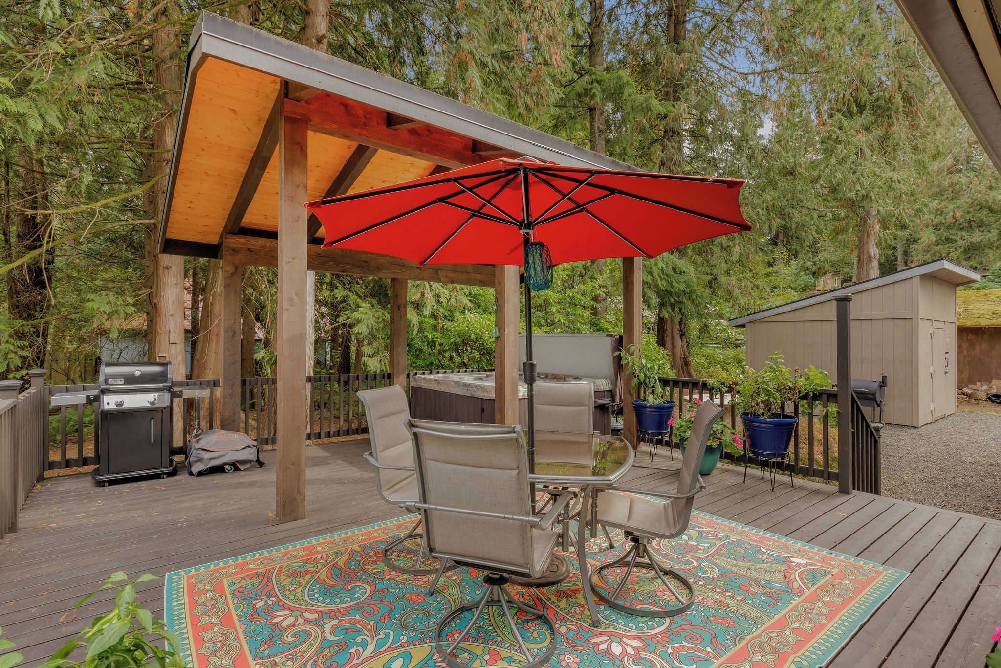 A covered outdoor patio with a grill, seating, and a red umbrella.