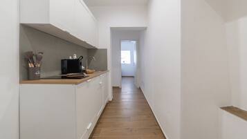 A narrow hallway with a kitchen area on the left, featuring cabinets, a microwave, and kitchen utensils.