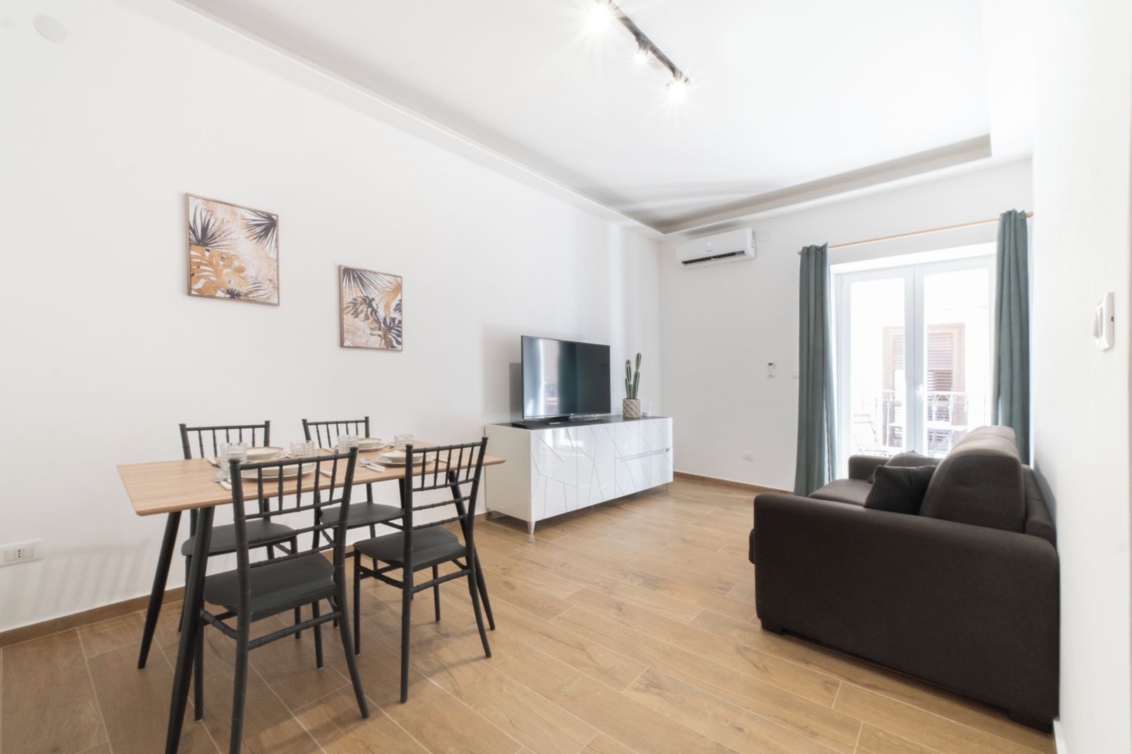 A modern living room with a dining area, a flat-screen TV, and a sofa.