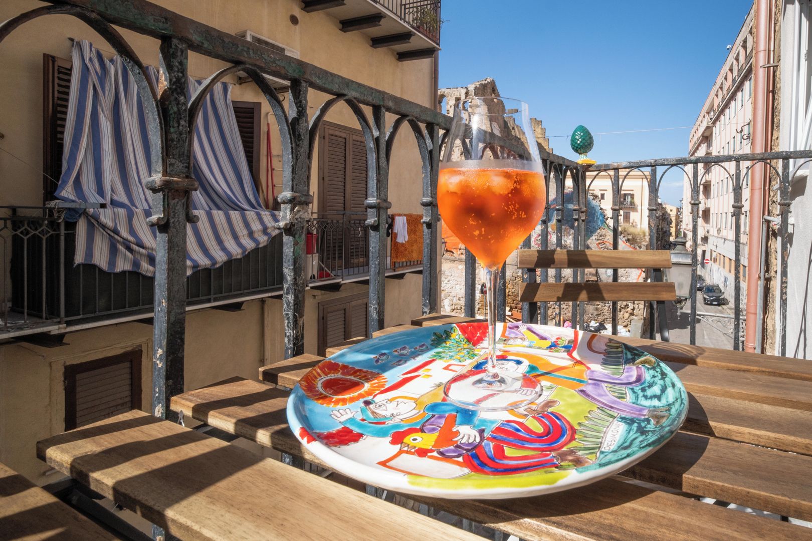 A colorful plate with a drink on a wooden table, set against a backdrop of a building with balconies and railings.