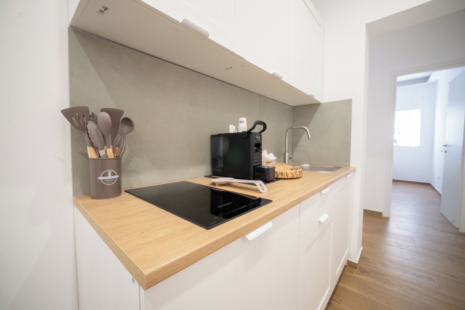 Une cuisine moderne dotée d’un plan de travail en bois, d’une plaque de cuisson à induction intégrée, d’une machine à café et d’un ensemble d’ustensiles de cuisine.