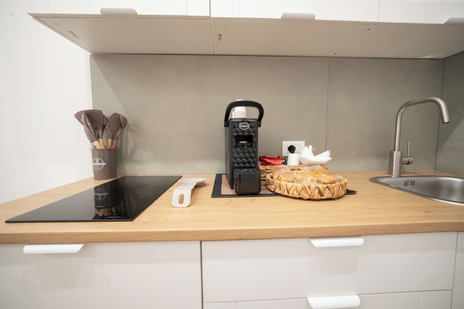 A modern kitchen with a built-in induction cooktop, a coffee machine, a cutting board, and a basket of bread.