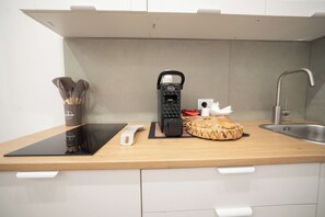 A modern kitchen with a built-in induction cooktop, a coffee machine, a cutting board, and a basket of bread. - New Listing (Palermo)