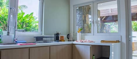 A kitchen with a sink, a coffee maker, and a window with a view of greenery.