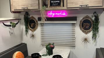 Een compacte kitchenette met een neonbord, een welkomstbord en decoratieve muurkunst.