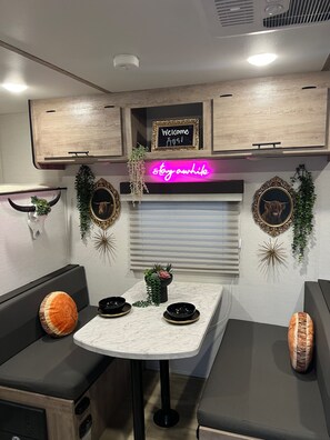 A compact kitchenette with a neon sign, a welcome sign, and decorative wall art.