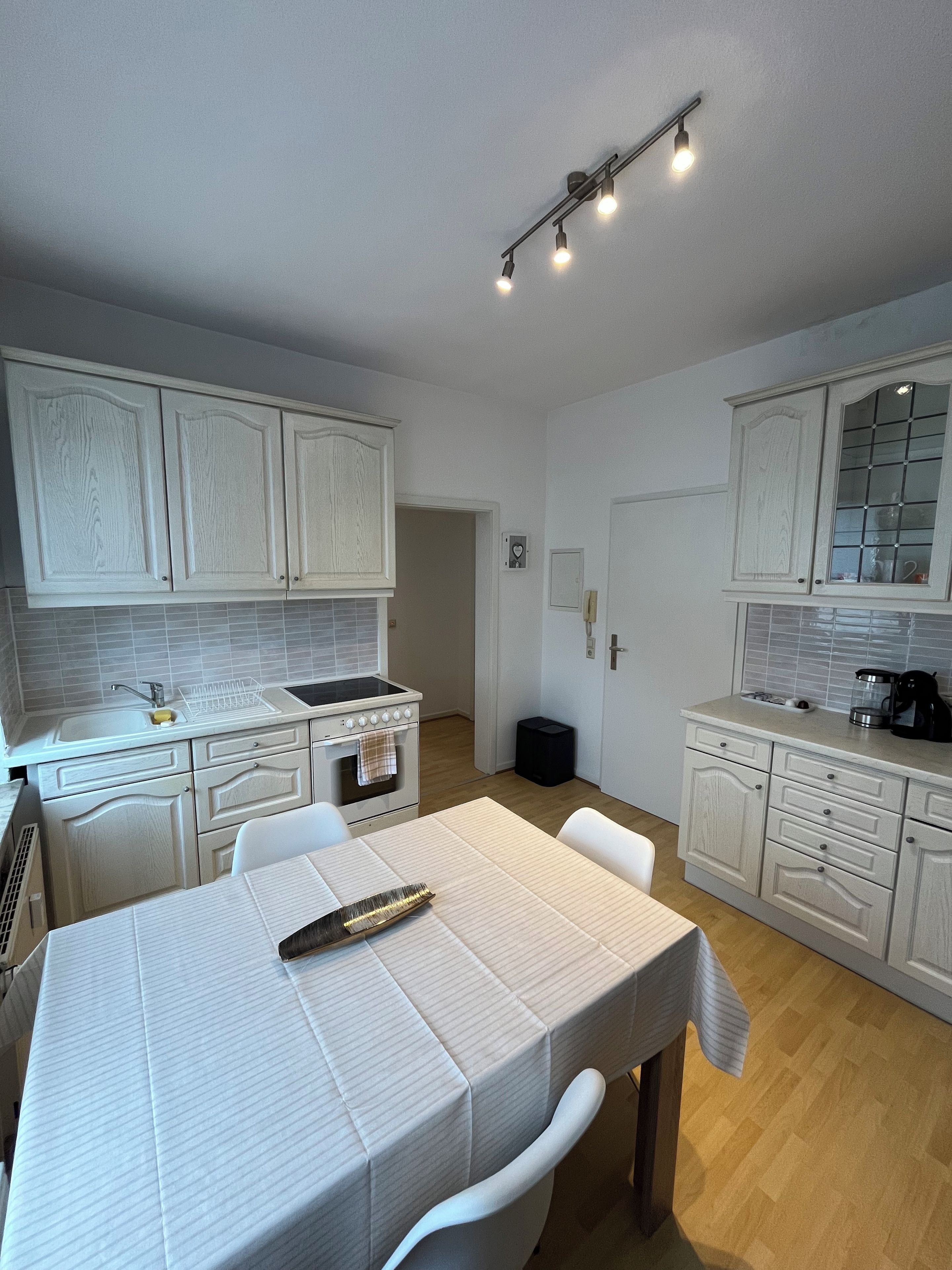 A modern kitchen with white cabinetry, a dining table with a placemat, and a built-in oven.