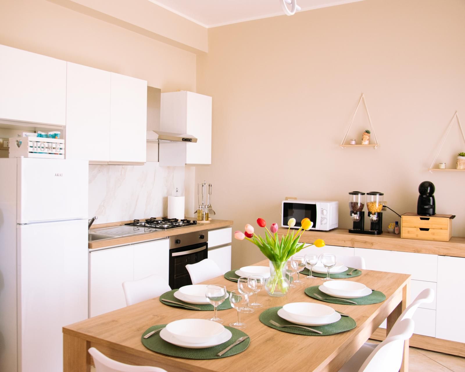 A modern kitchen with white cabinets, a gas stove, and a dining area set for four with green placemats and white plates.