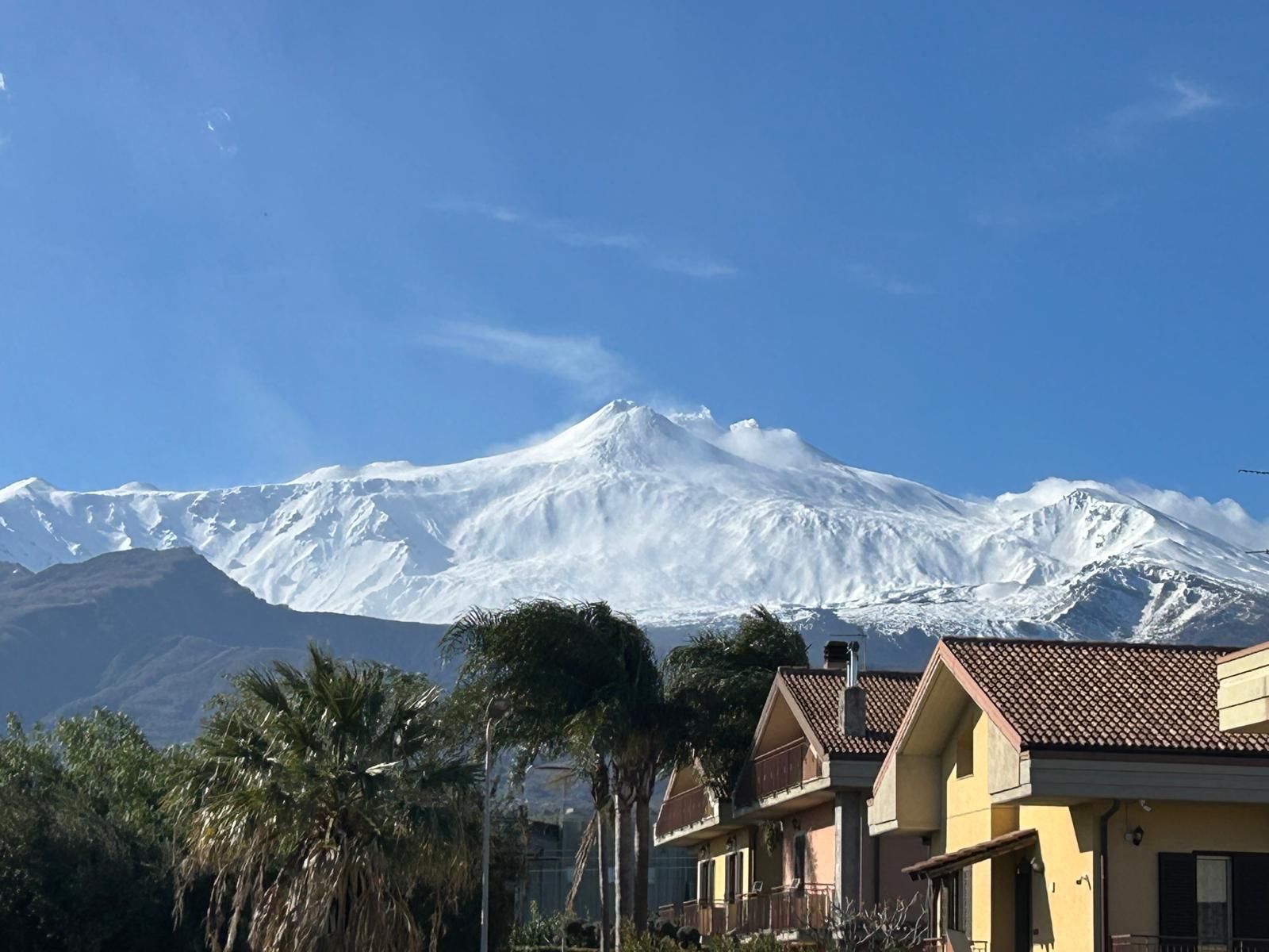 Montanha coberta de neve com céu límpido, rodeada por edifícios residenciais com varandas visíveis.