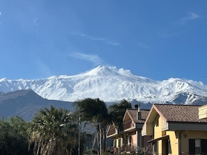 Montanha coberta de neve com céu límpido, rodeada por edifícios residenciais com varandas visíveis.