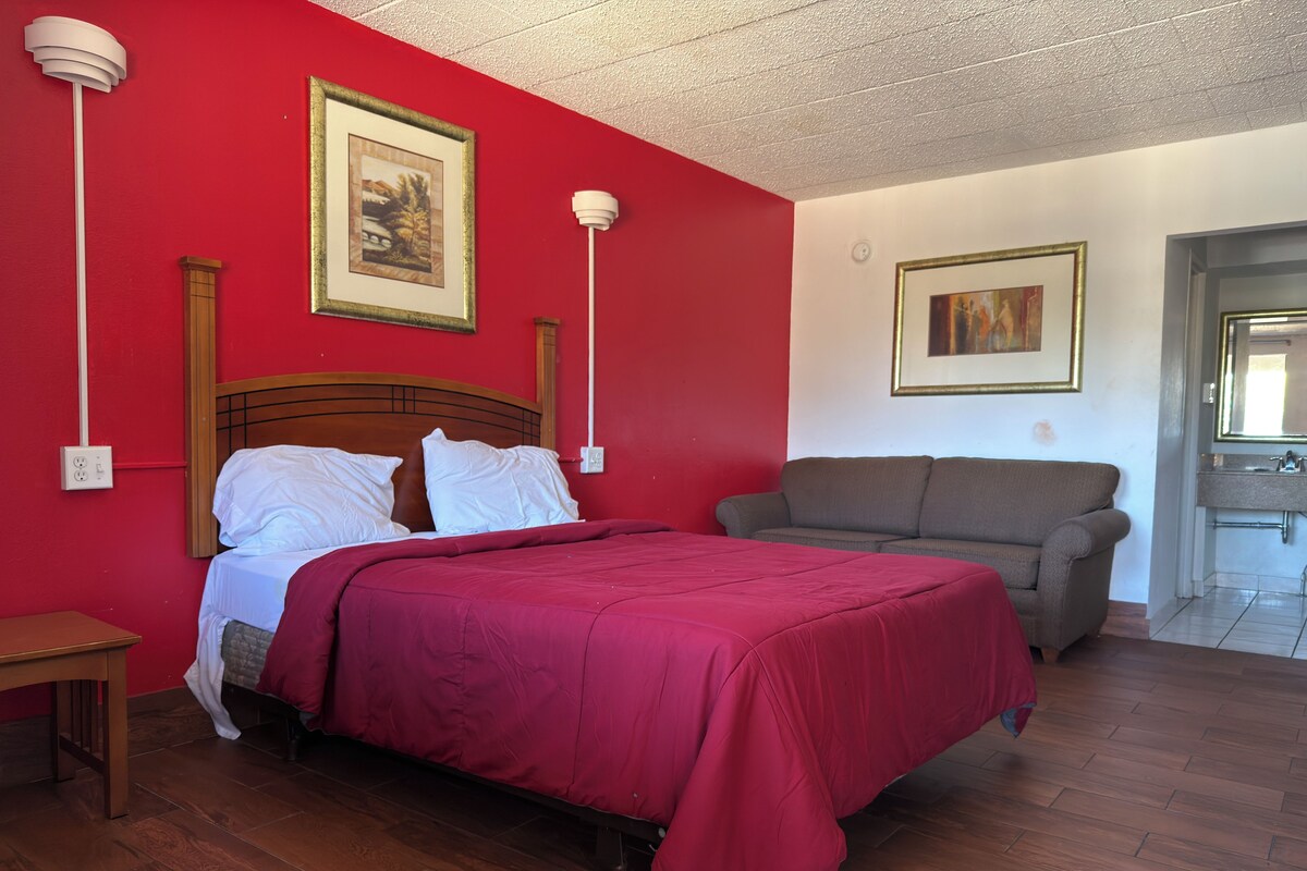Una habitación con cama, sofá, piso de madera y un baño visible a través de una puerta abierta.