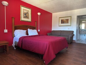 Una habitación con cama, sofá, piso de madera y un baño visible a través de una puerta abierta.