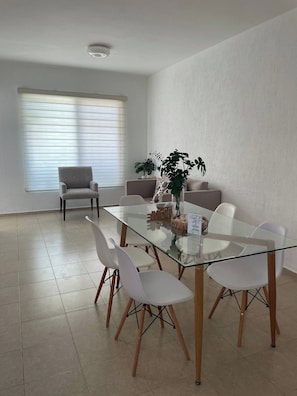 Een moderne eethoek met een glazen tafel, witte stoelen en een potplant.