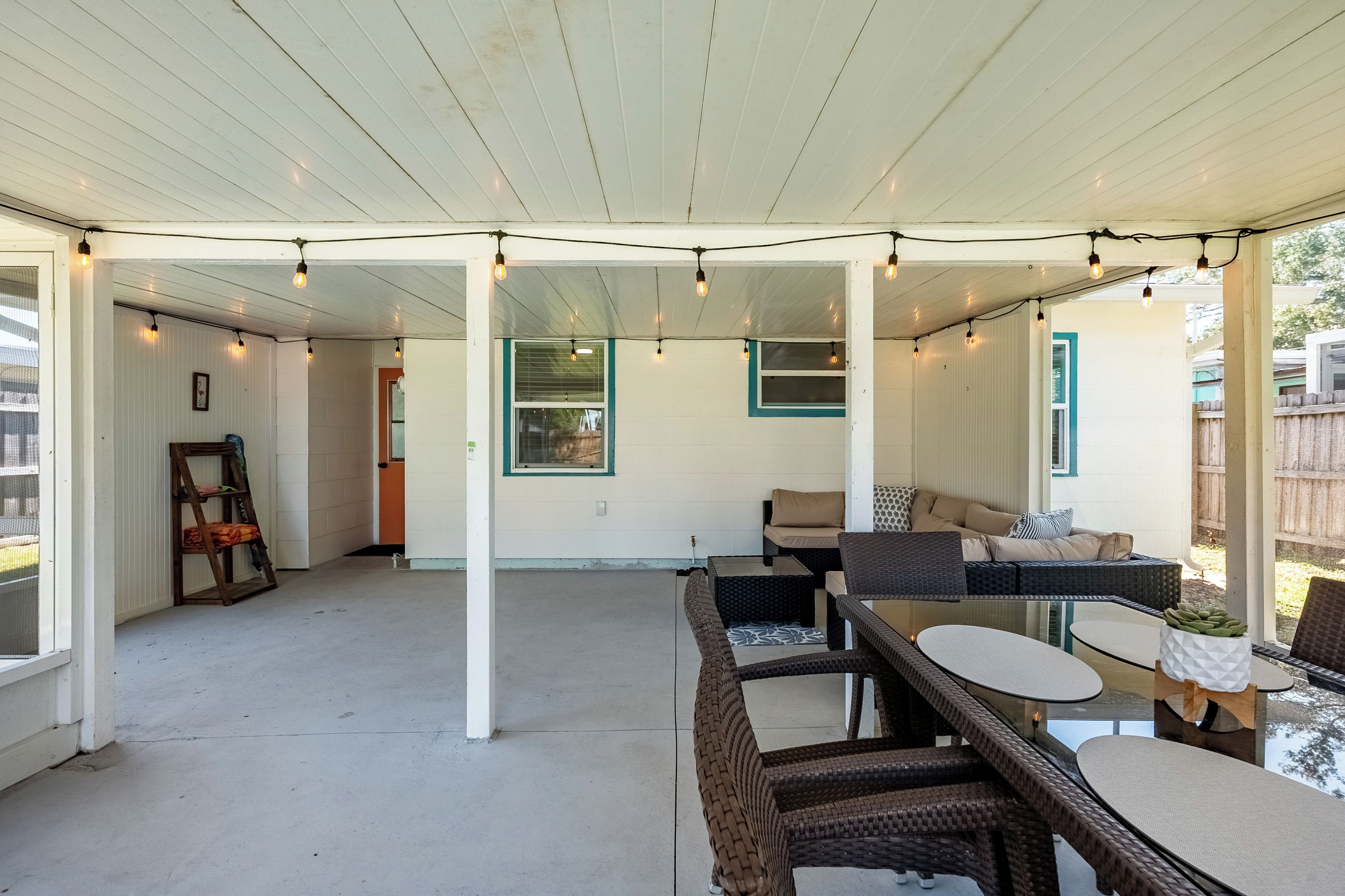 A covered patio area with wicker furniture, string lights, and a view of the backyard.