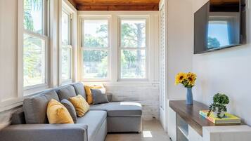 A room with a grey sectional sofa, a wooden ceiling, and a TV mounted on the wall.