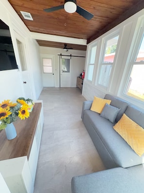 Un interior moderno con un sofá gris, un ventilador de techo y techo de madera.