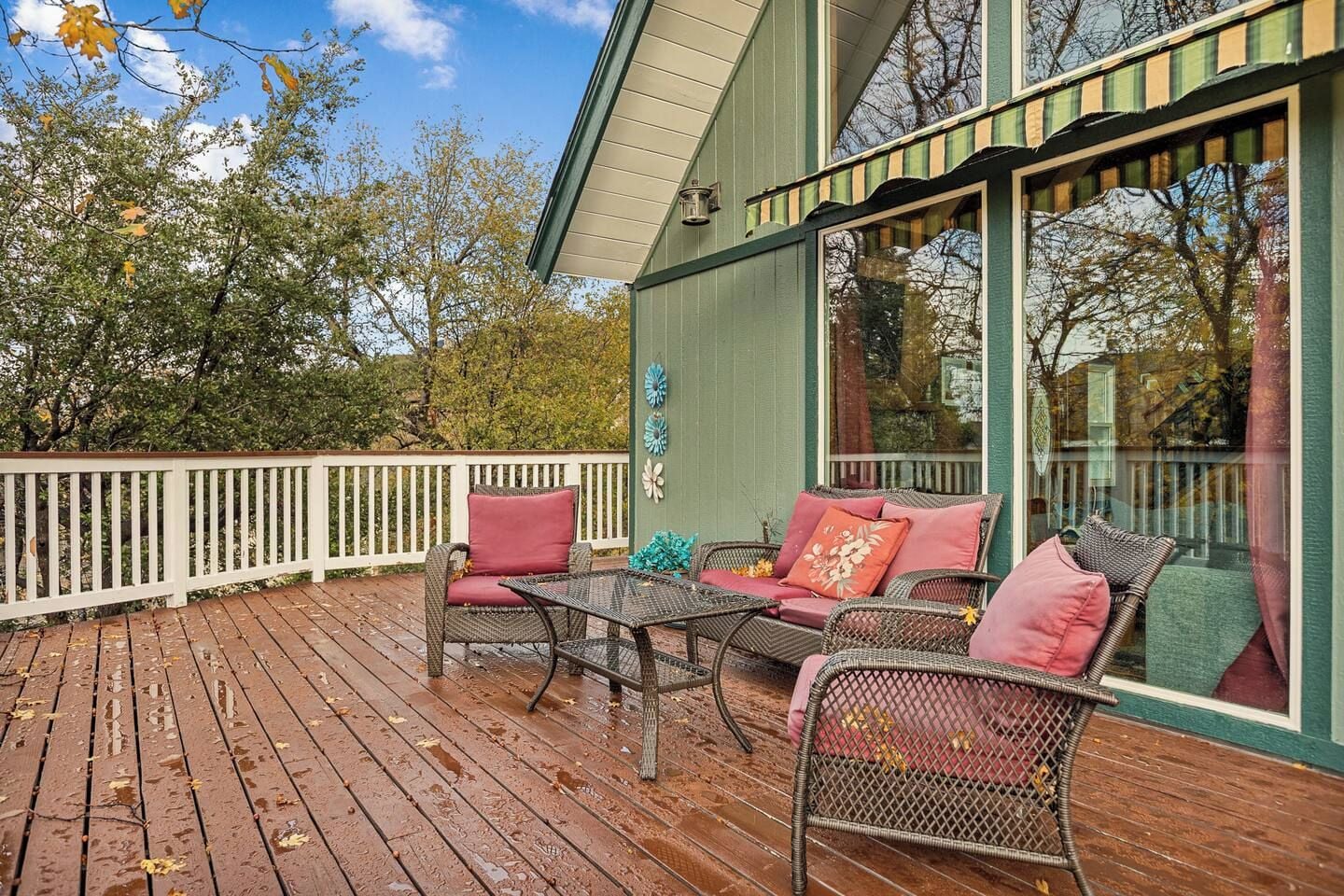 A wooden deck with outdoor furniture, a white fence, and a building with large windows.