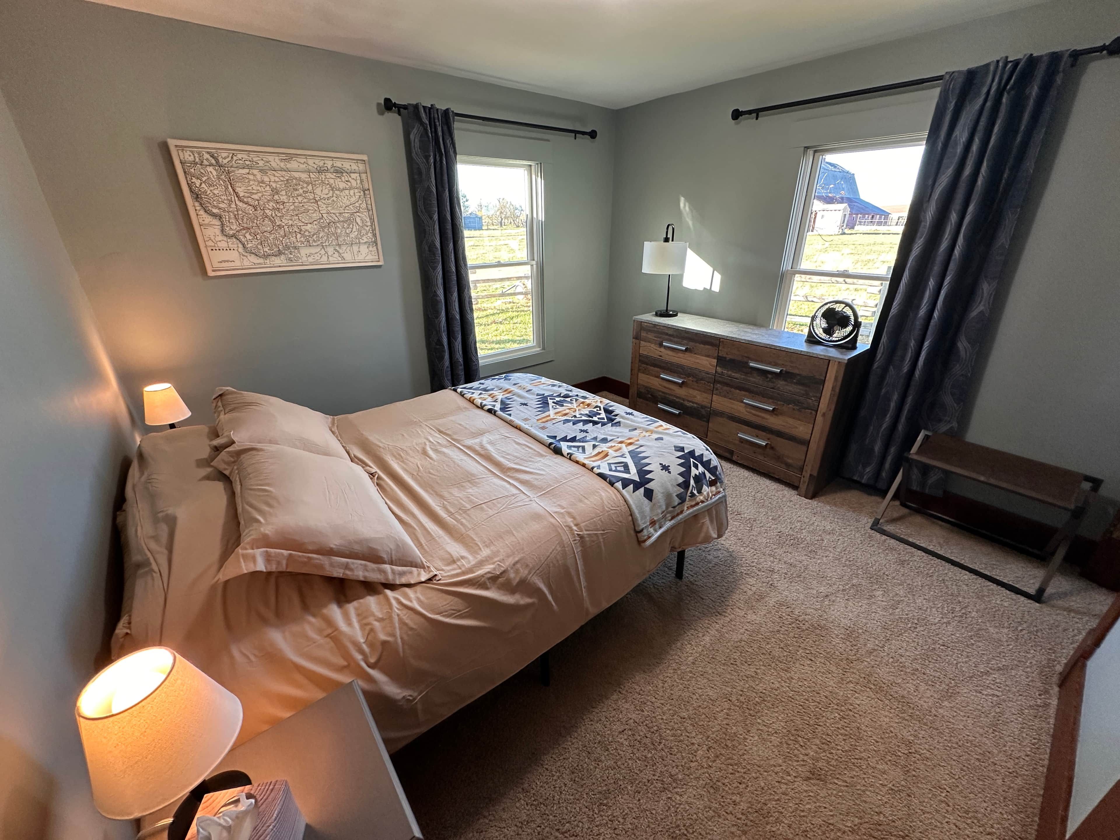 Une chambre à coucher avec un lit, une commode, une lampe et une carte accrochée au mur.