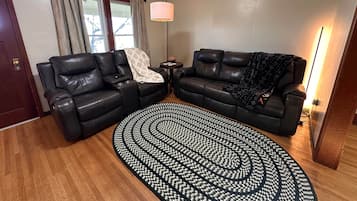 A living room with a black leather sofa, a patterned rug, a lamp, and a window with curtains.