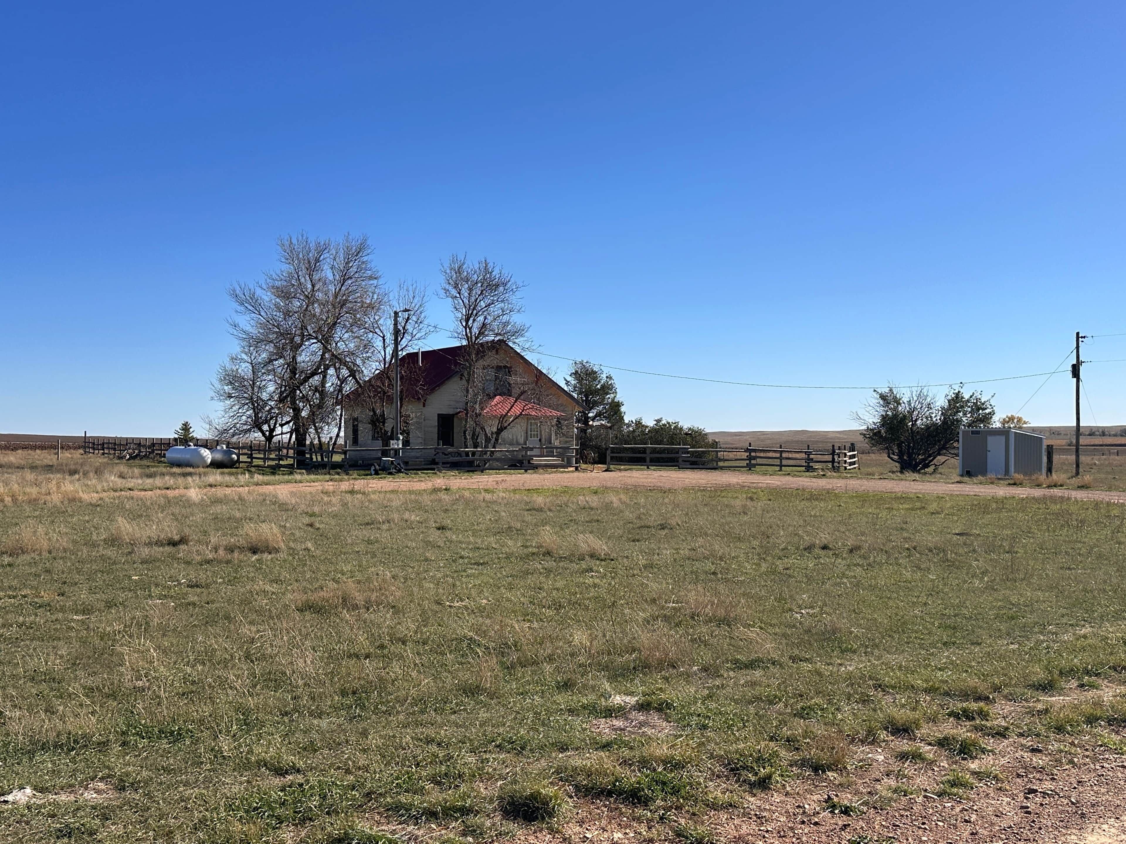 A rural landscape with a single house, a fenced area, and a clear sky.