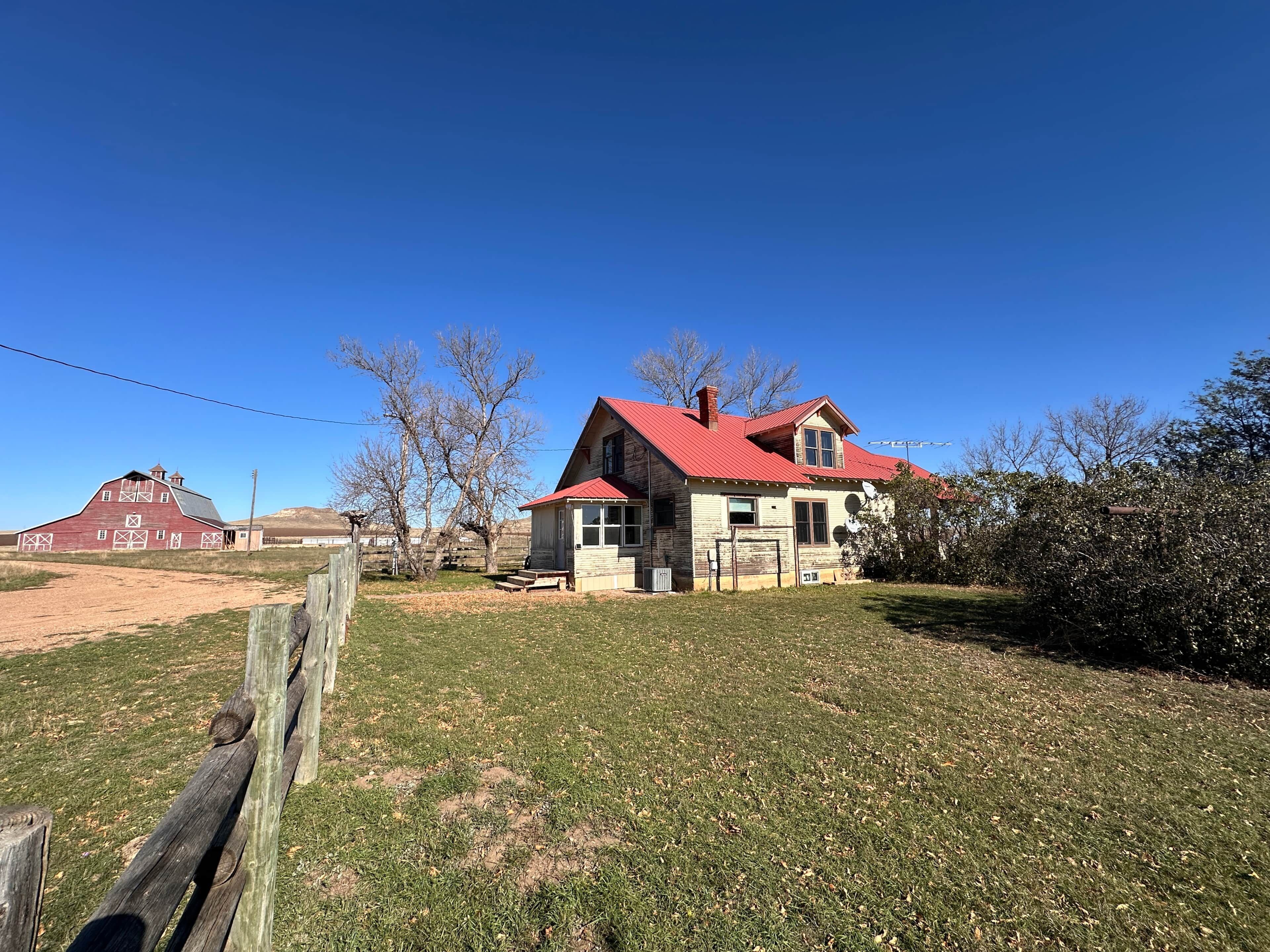 A rural property with a red barn, a two-story house with a red roof, and a grassy yard.