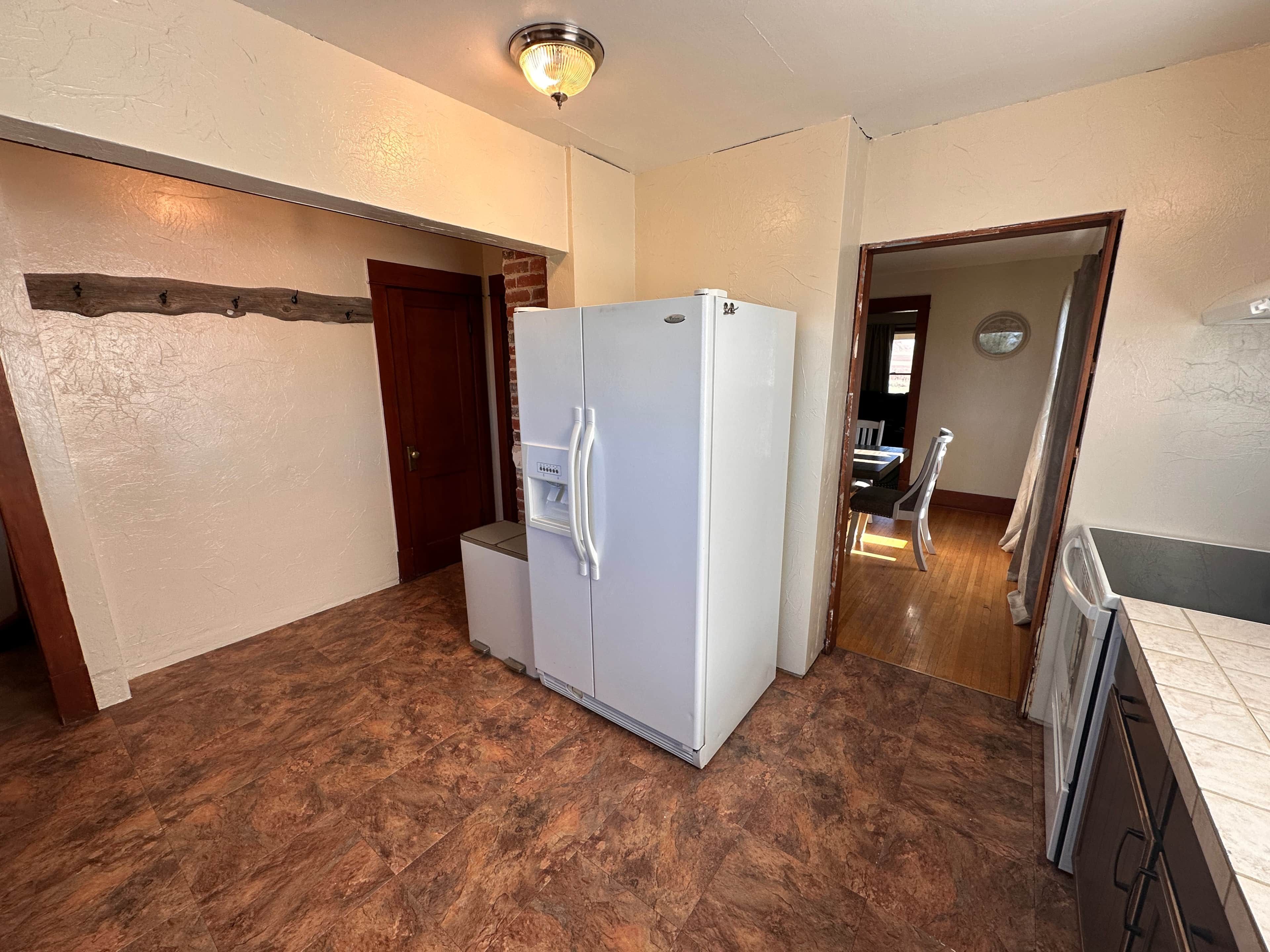 A kitchen with a refrigerator, a small countertop, and a door leading to another room.