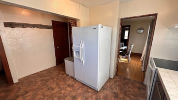 A kitchen with a refrigerator, a small countertop, and a door leading to another room.