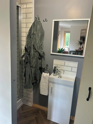 A bathroom with a shower, a sink with a mirror above it, and a towel hanging on a hook.