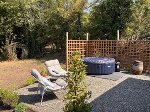 Ein Garten mit zwei Liegestühlen, einem Whirlpool und einem Holzfass.