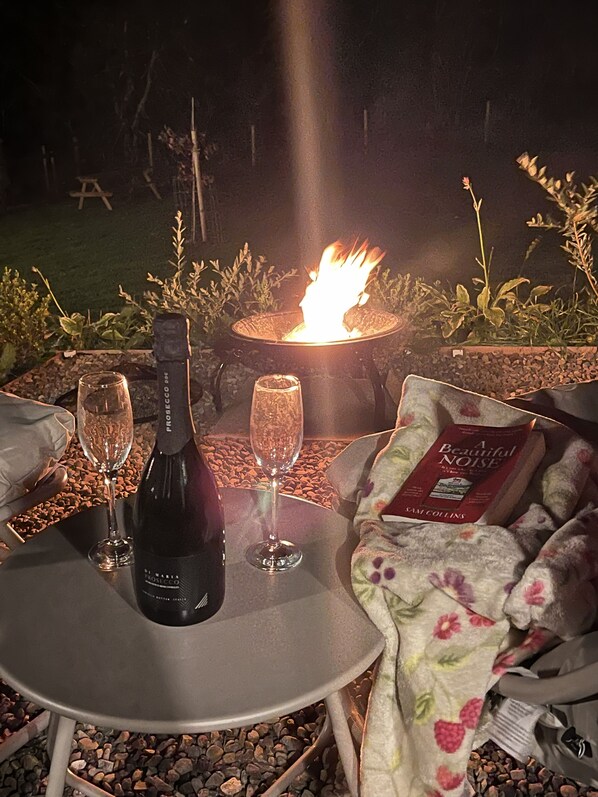 A table with a bottle of wine, two glasses, and a blanket with a floral pattern.