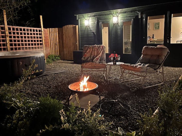 An outdoor seating area with a fire pit, lounge chairs, and a small table with drinks.