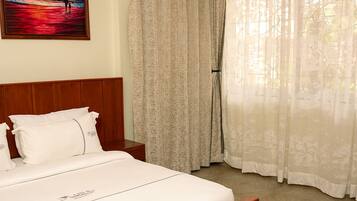 Ein Schlafzimmer mit einem hölzernen Bett, weißer Bettwäsche, einem Nachttisch, einem Gemälde und leichten Vorhängen.