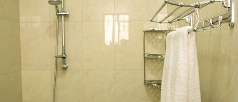 A shower with a handheld showerhead and a towel rack with a white towel.