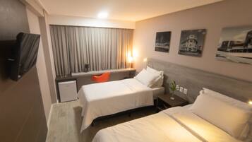 Quarto de hotel com duas camas, uma escrivaninha, uma cadeira, uma televisão e obras de arte nas paredes.