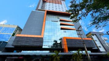 Um edifício moderno com fachada de vidro, esquema de cores predominante em laranja e cinza, e uma área de entrada visível com uma placa.