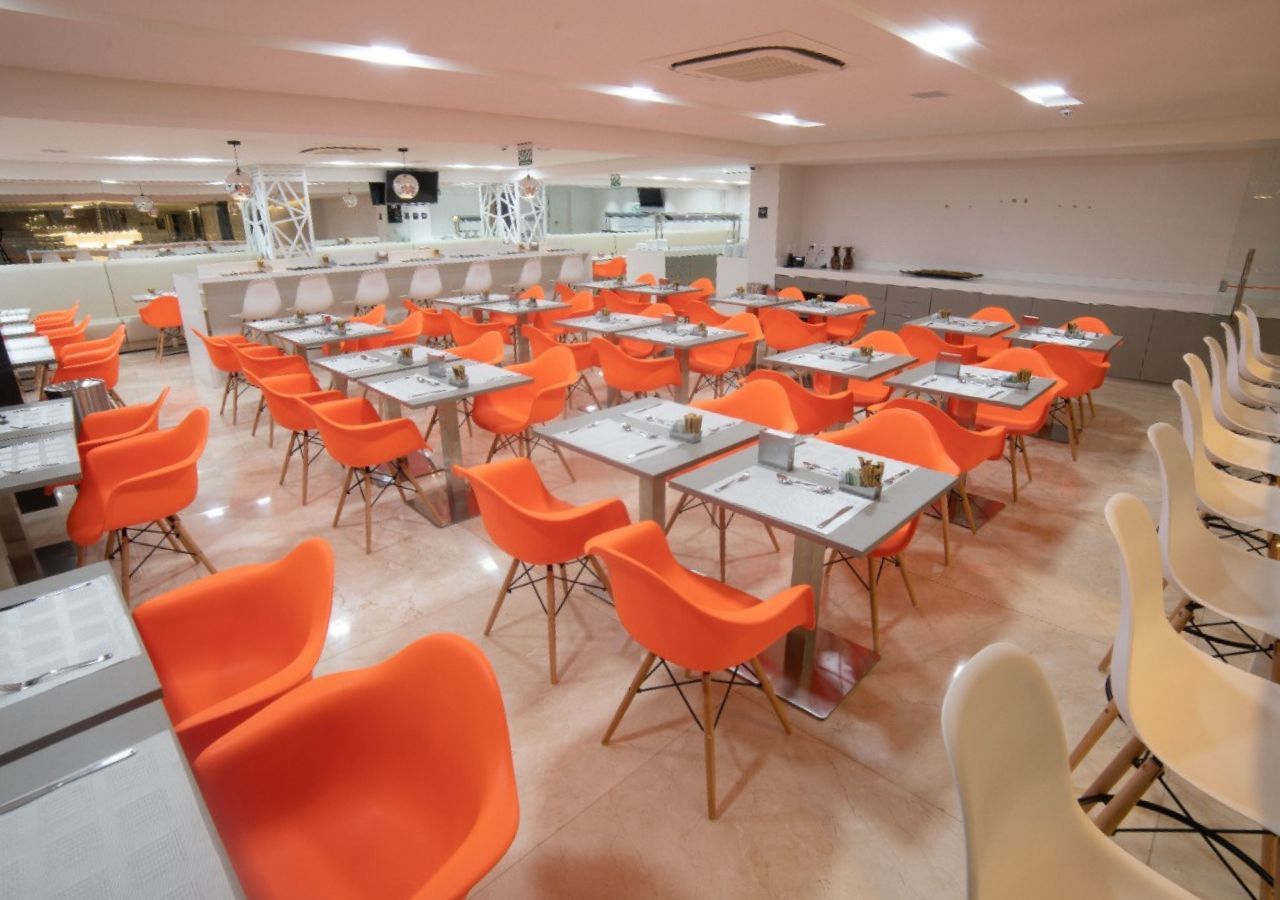 A dining area with multiple tables and chairs, a kitchen in the background, and a clean, modern interior.