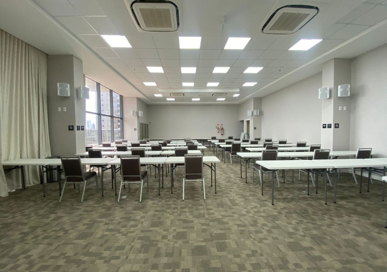 A conference room with multiple tables and chairs, air conditioning units, and a large window.