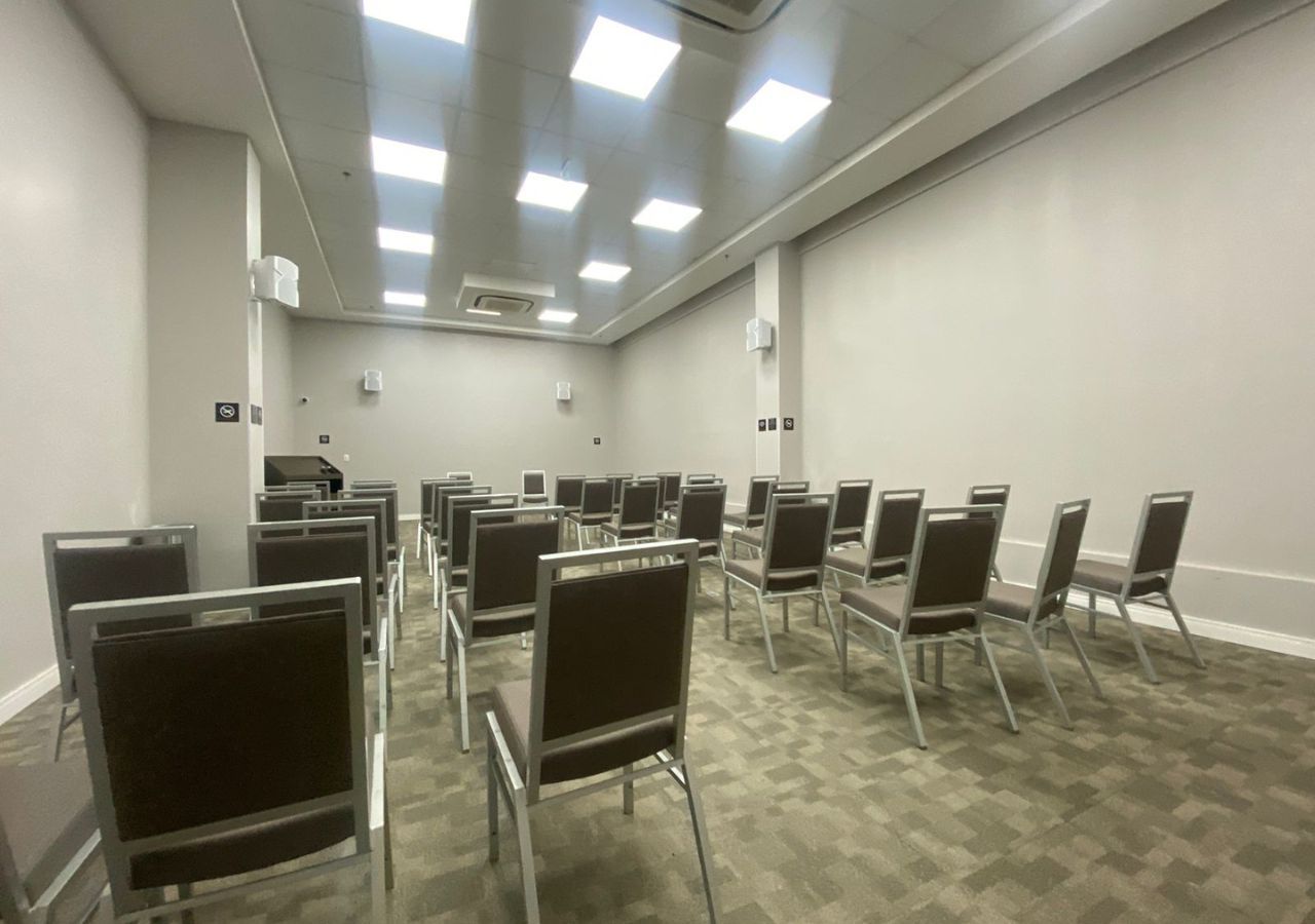A conference room with rows of chairs and tables, equipped with ceiling lights and air conditioning units.