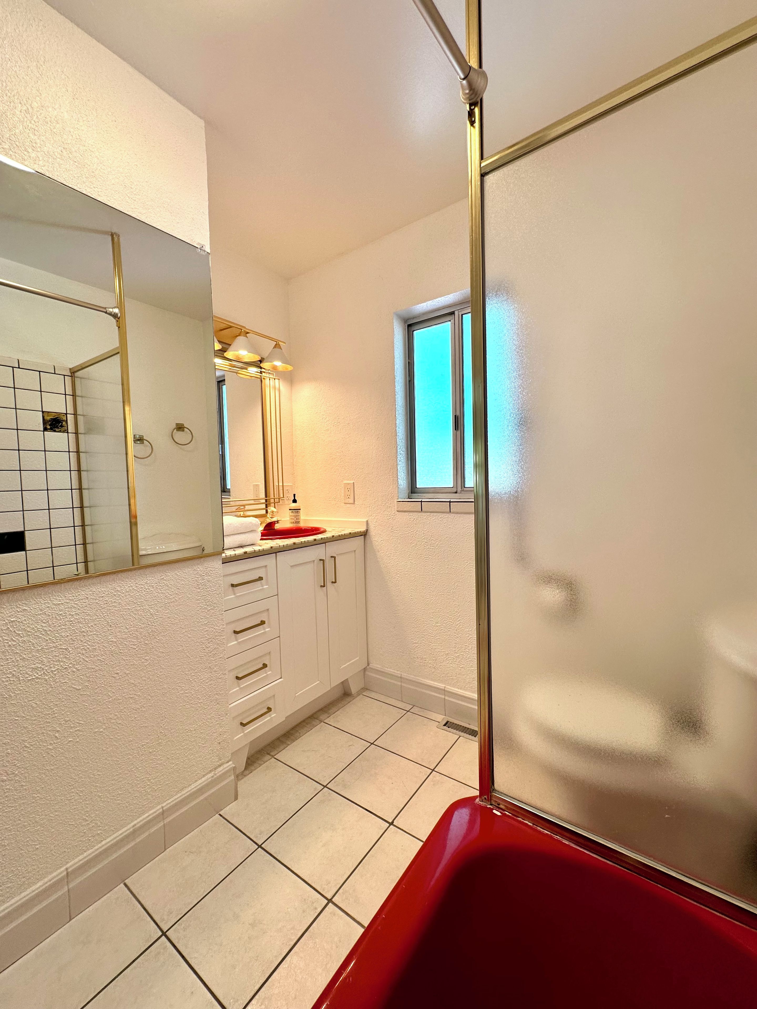 Ein Badezimmer mit einer roten Badewanne, weißen Fliesen, einem großen Spiegel, einem Fenster und einem Handtuchhalter.