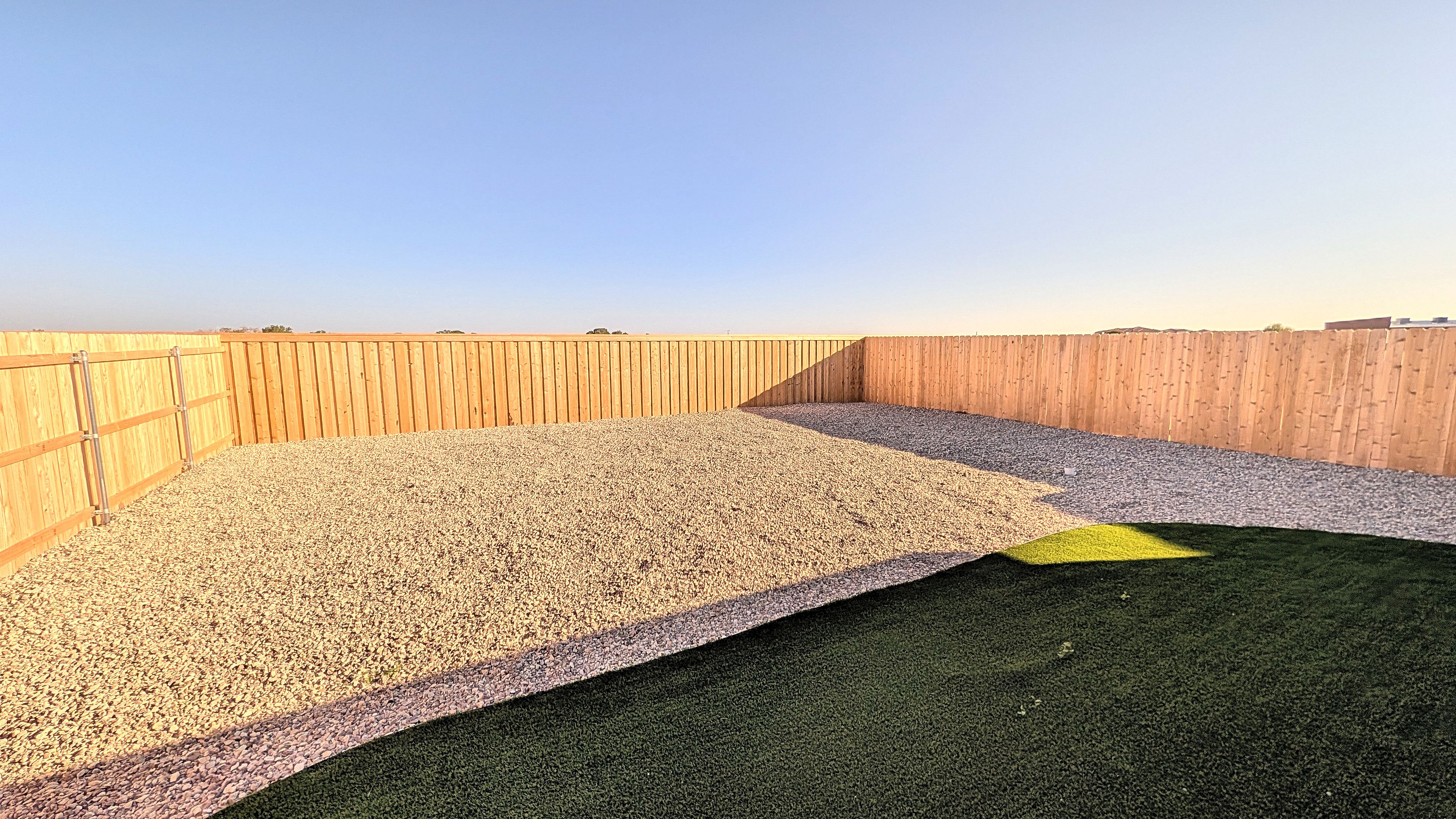 A rooftop terrace with a wooden fence, gravel flooring, and a section of artificial grass.