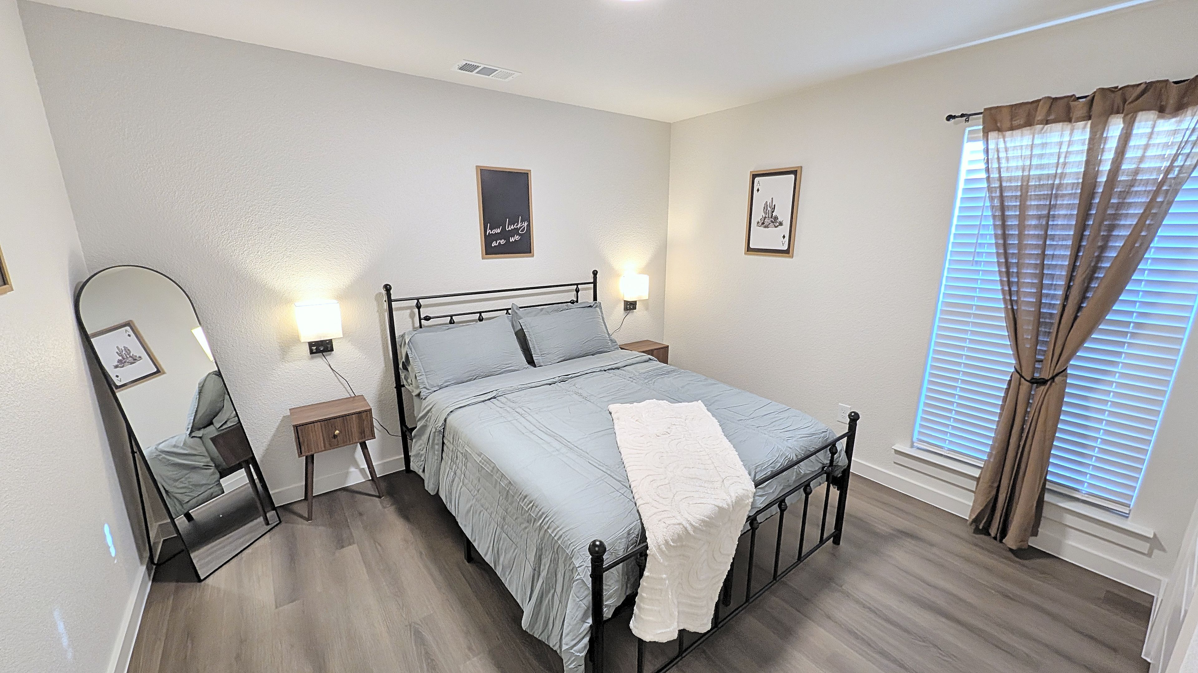 A bedroom with a bed, bedside tables, a mirror, and a window with curtains.