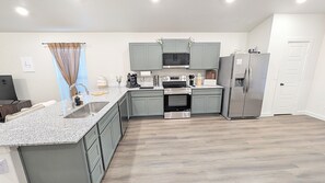 A modern kitchen with granite countertops, stainless steel appliances, and light gray cabinetry. - Modern 3BR Auburn St. Retreat (Lubbock)