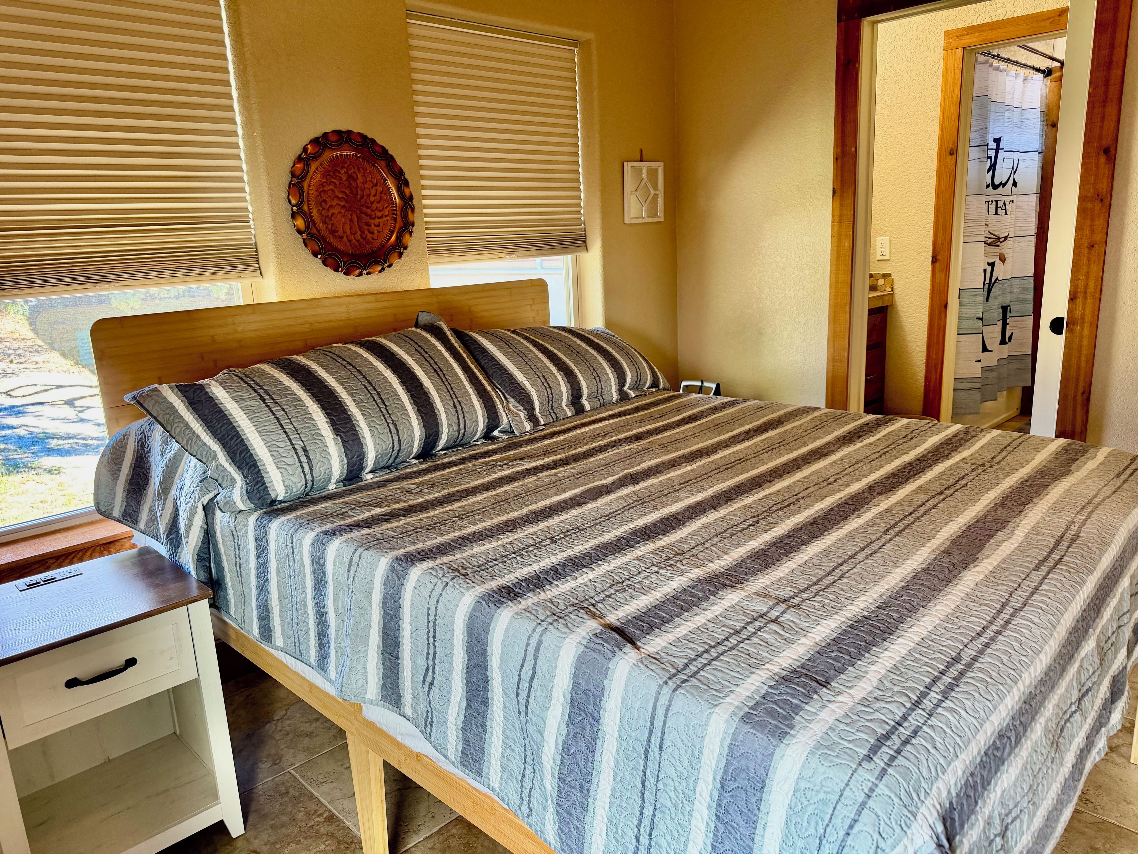 Una cama con colcha a rayas, cabecera de madera y mesita de noche con cajón.