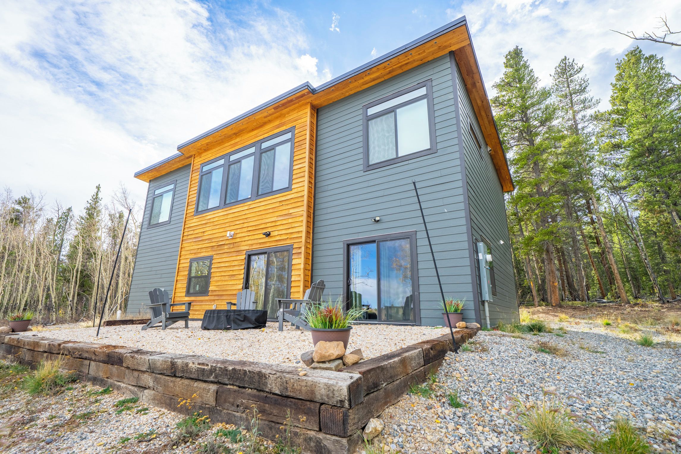 A two-story modern house with a combination of grey and yellow siding, large windows, and a gravel driveway.