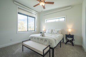 Ein Schlafzimmer mit einem Bett, Nachttischen, einem Deckenventilator und Fenstern.